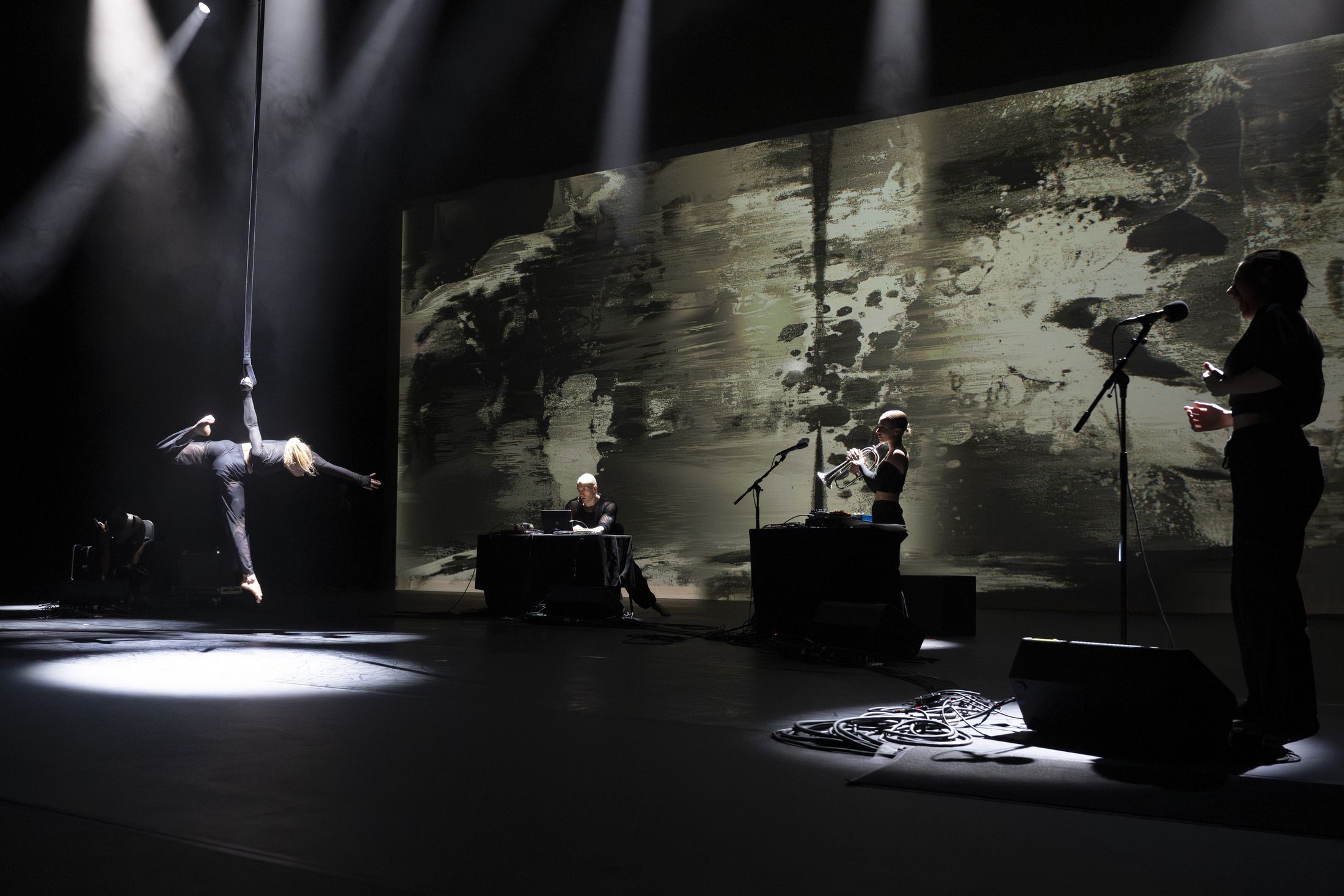 The aerialist suspended in a shaft of light above the stage, the projection wall behind